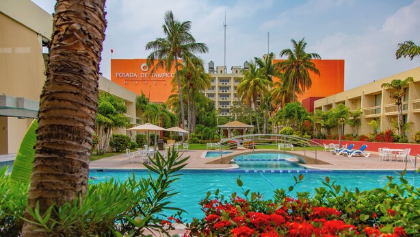 Ein Hotelpoolbereich mit Palmen, einer Brücke und Liegestühlen.