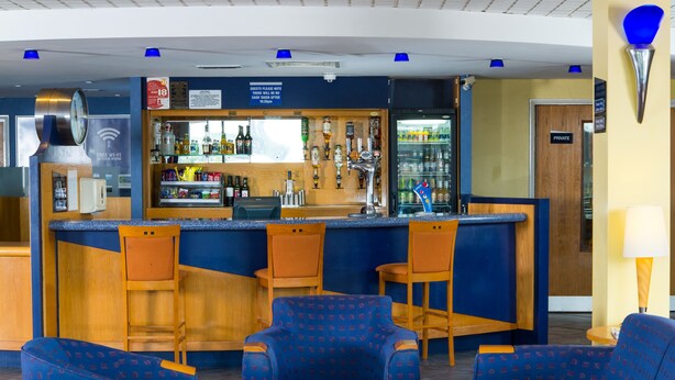 Zona de bar con asientos, un reloj y un cartel que indica conexión Wi-Fi gratuita.