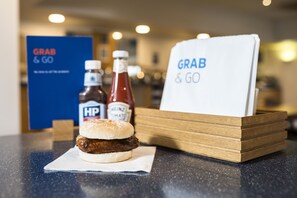 A sandwich on a napkin, two condiment bottles, and a 'Grab & Go' sign on a counter.