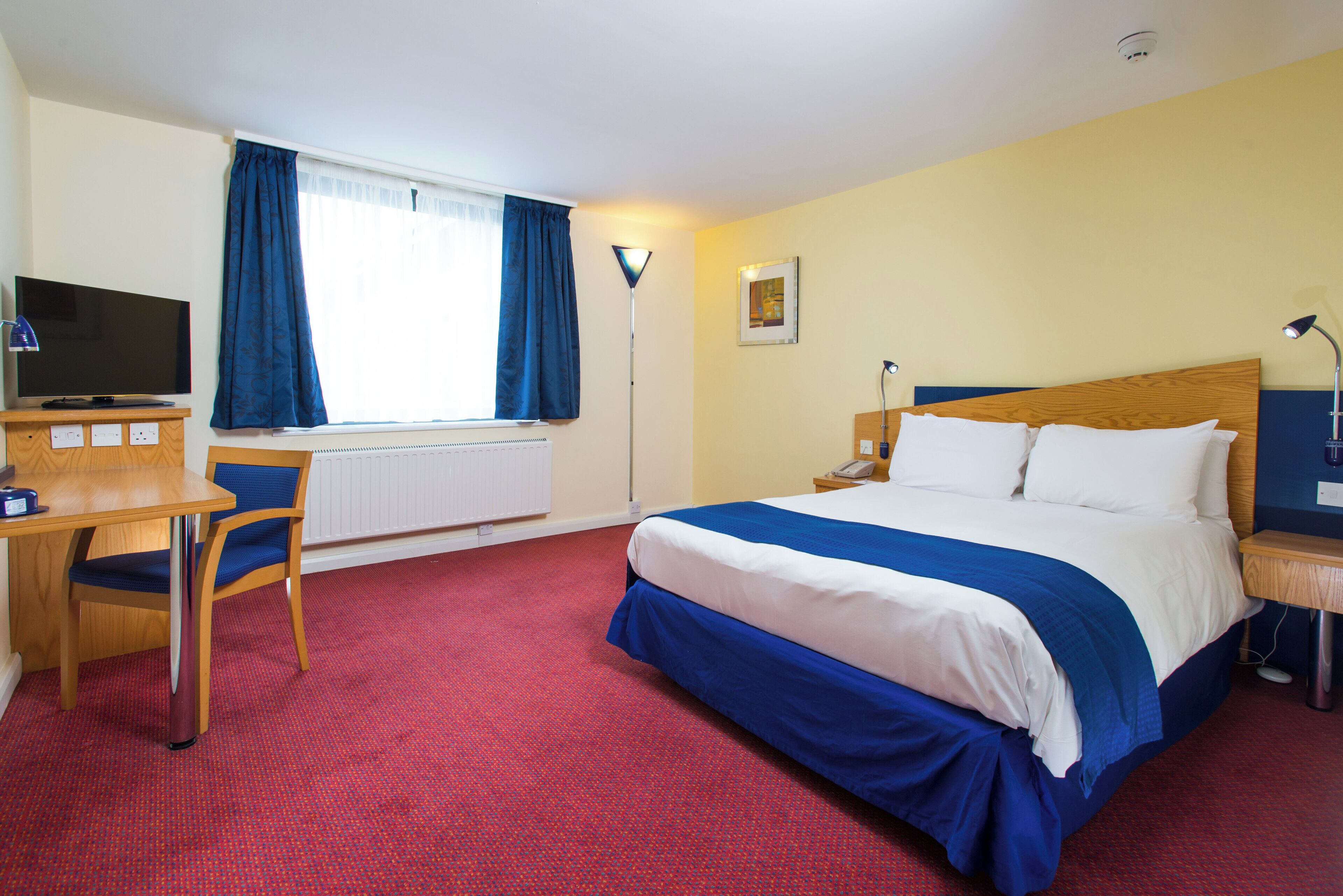 A hotel room with a bed, desk, chair, and a television.