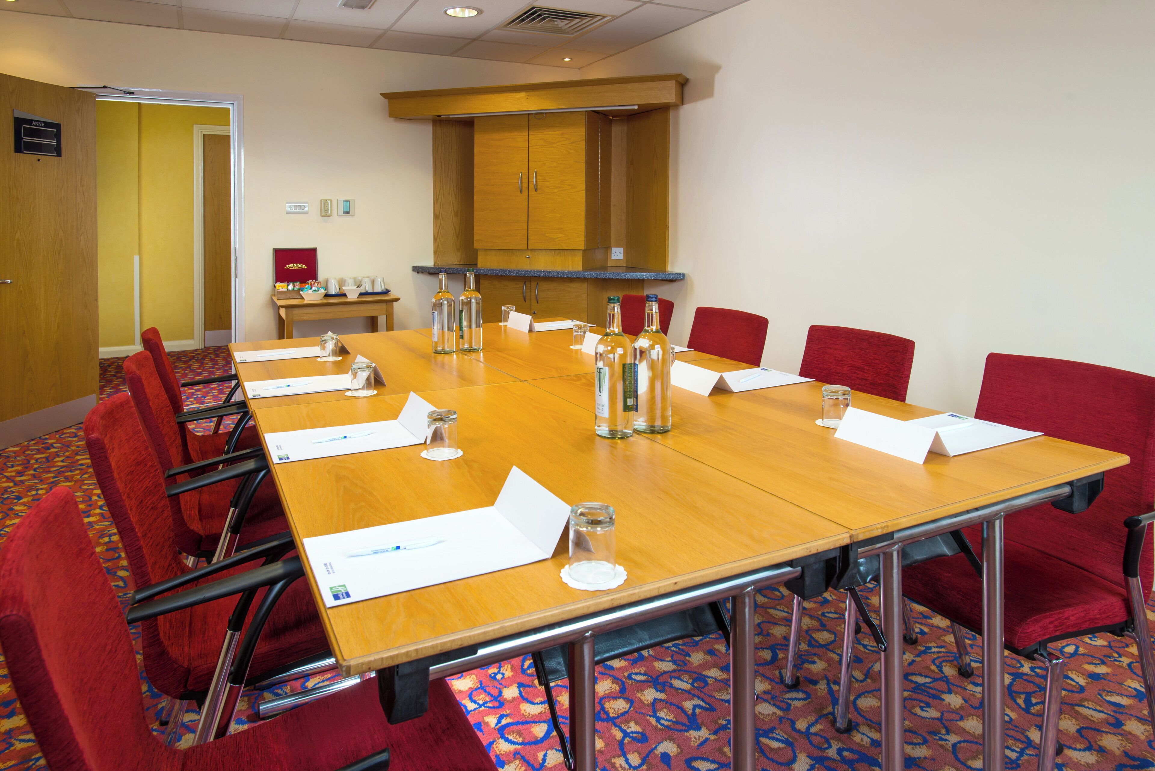 A conference room with a long table, red chairs, name cards, and water bottles.
