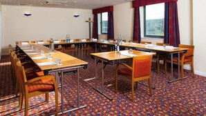 Un salón de conferencias con una mesa larga, sillas y una alfombra estampada.