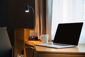 Una laptop sobre un escritorio de madera, con una taza blanca a un lado, una lámpara y una silla.