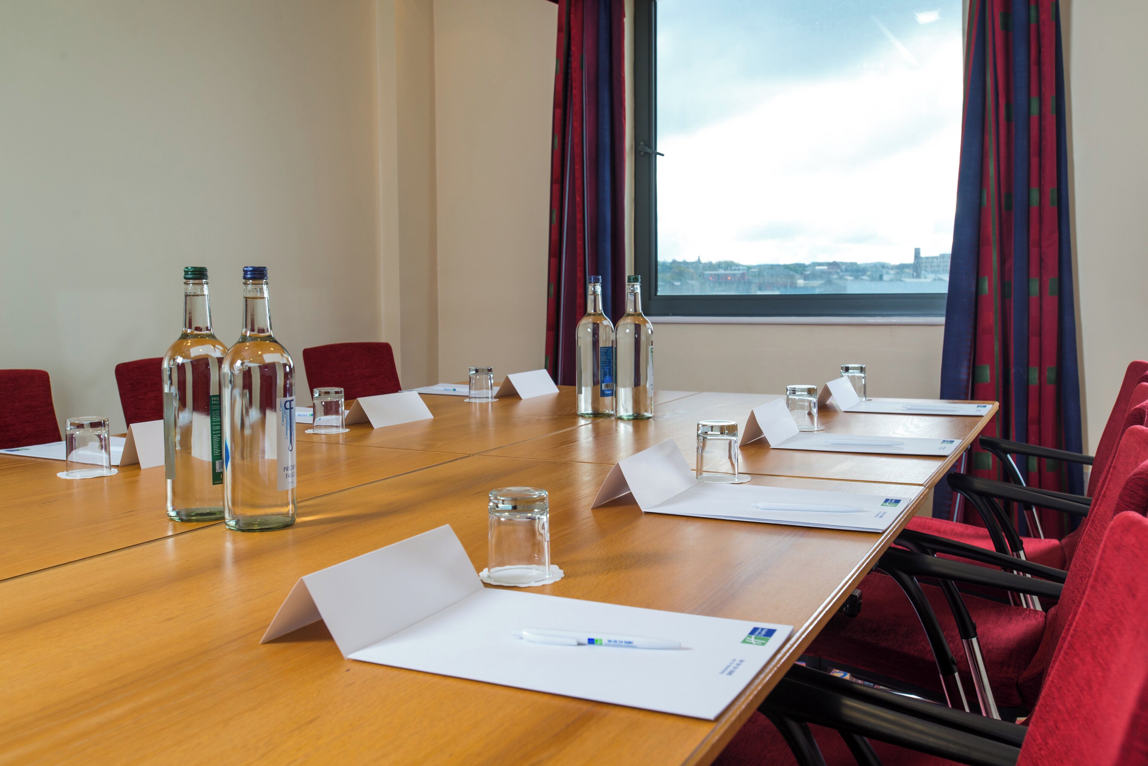 A conference room with a long table, red chairs, and bottles of water.