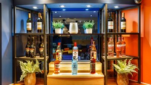 A bar area with shelves of liquor bottles, potted plants, and a wooden counter.