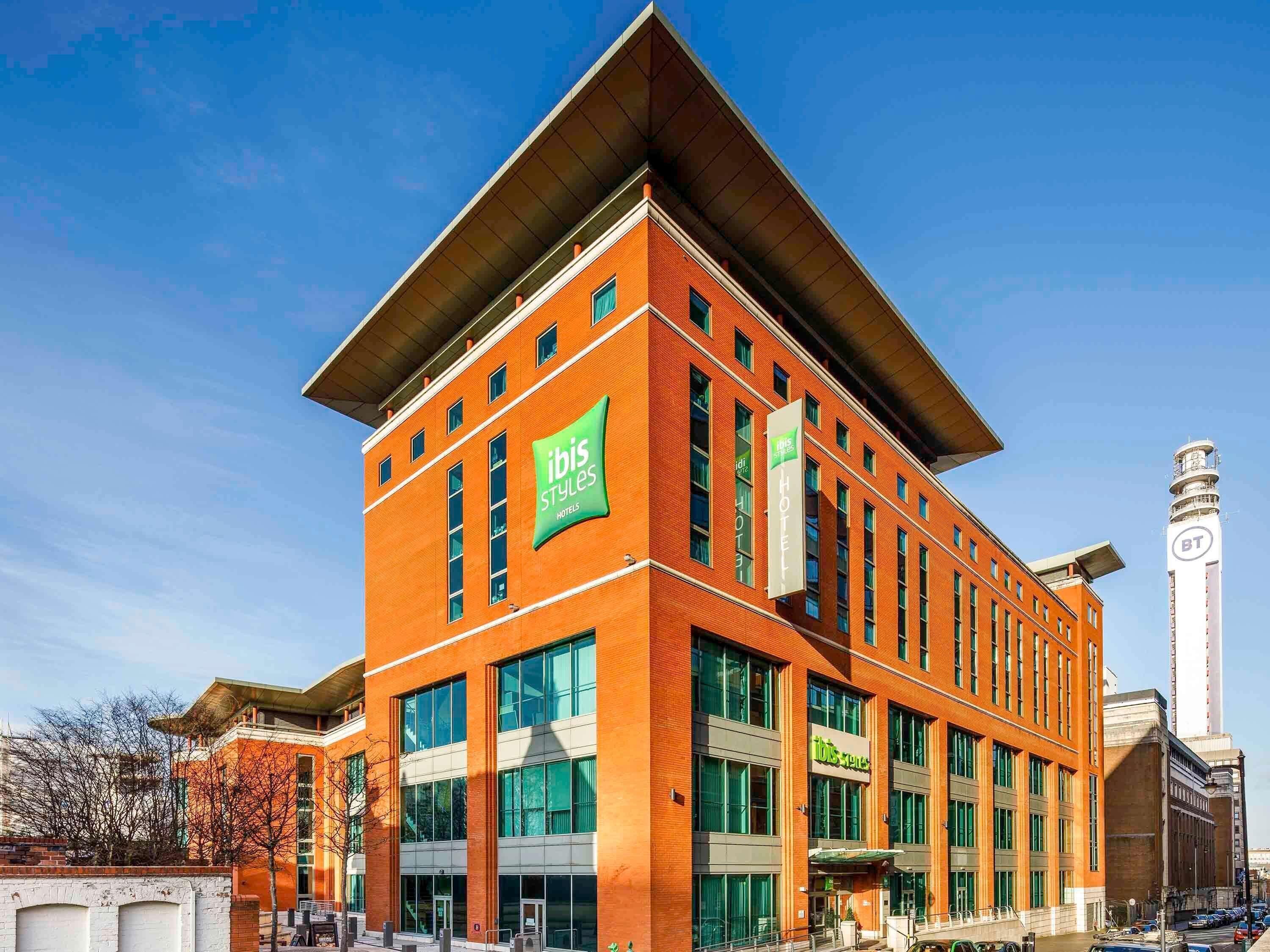 A modern hotel with a prominent 'ibis Styles' sign, large windows, and a tall tower with 'BT' branding.
