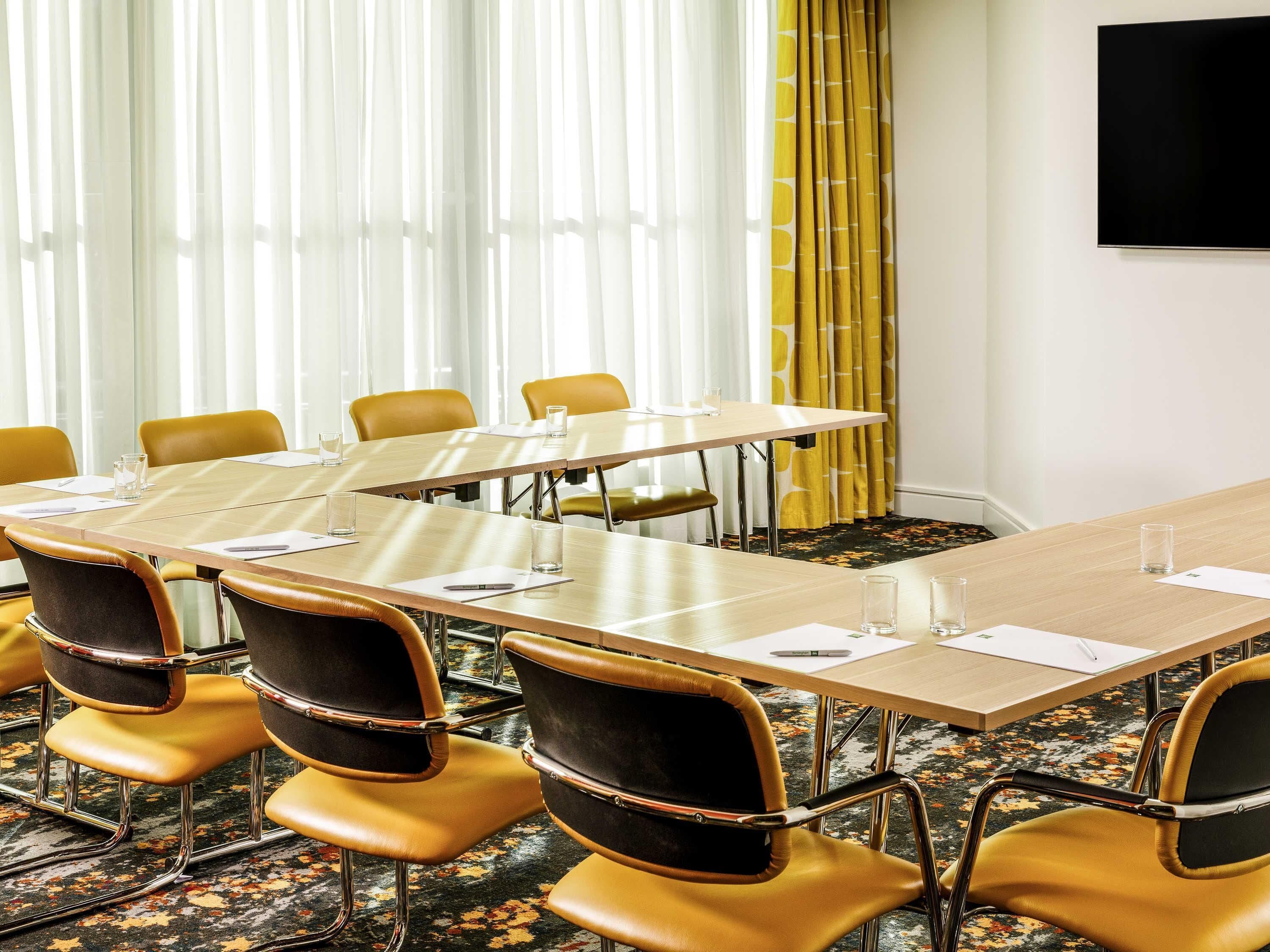 A conference room with a long table, chairs, a TV, and a window with curtains.