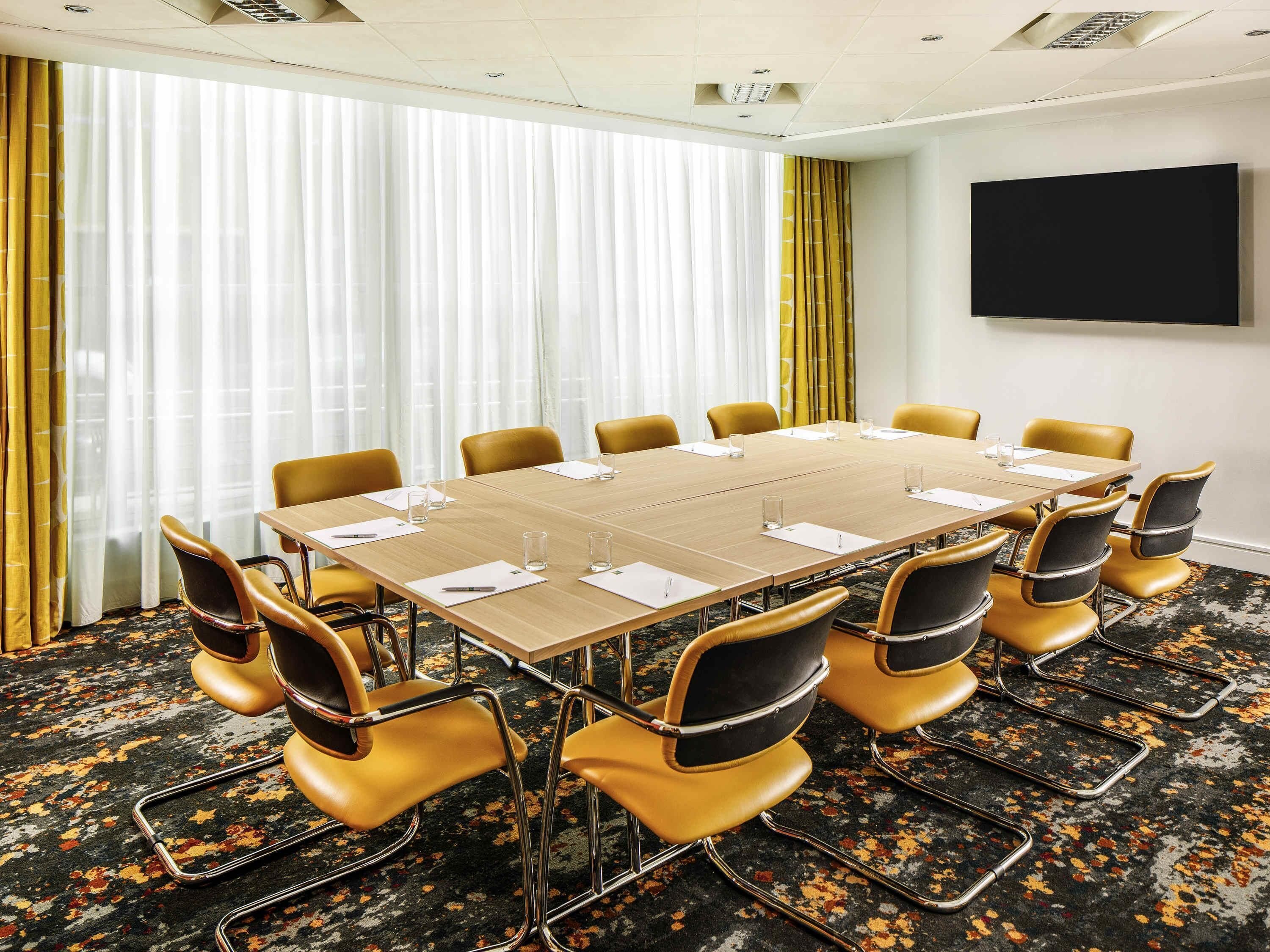 Un salón de conferencias con una larga mesa, sillas amarillas y una pantalla grande en la pared.