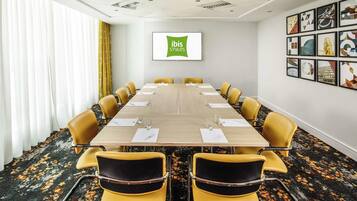 A conference room with a long table, yellow chairs, and a 'ibis Styles' sign on the wall.