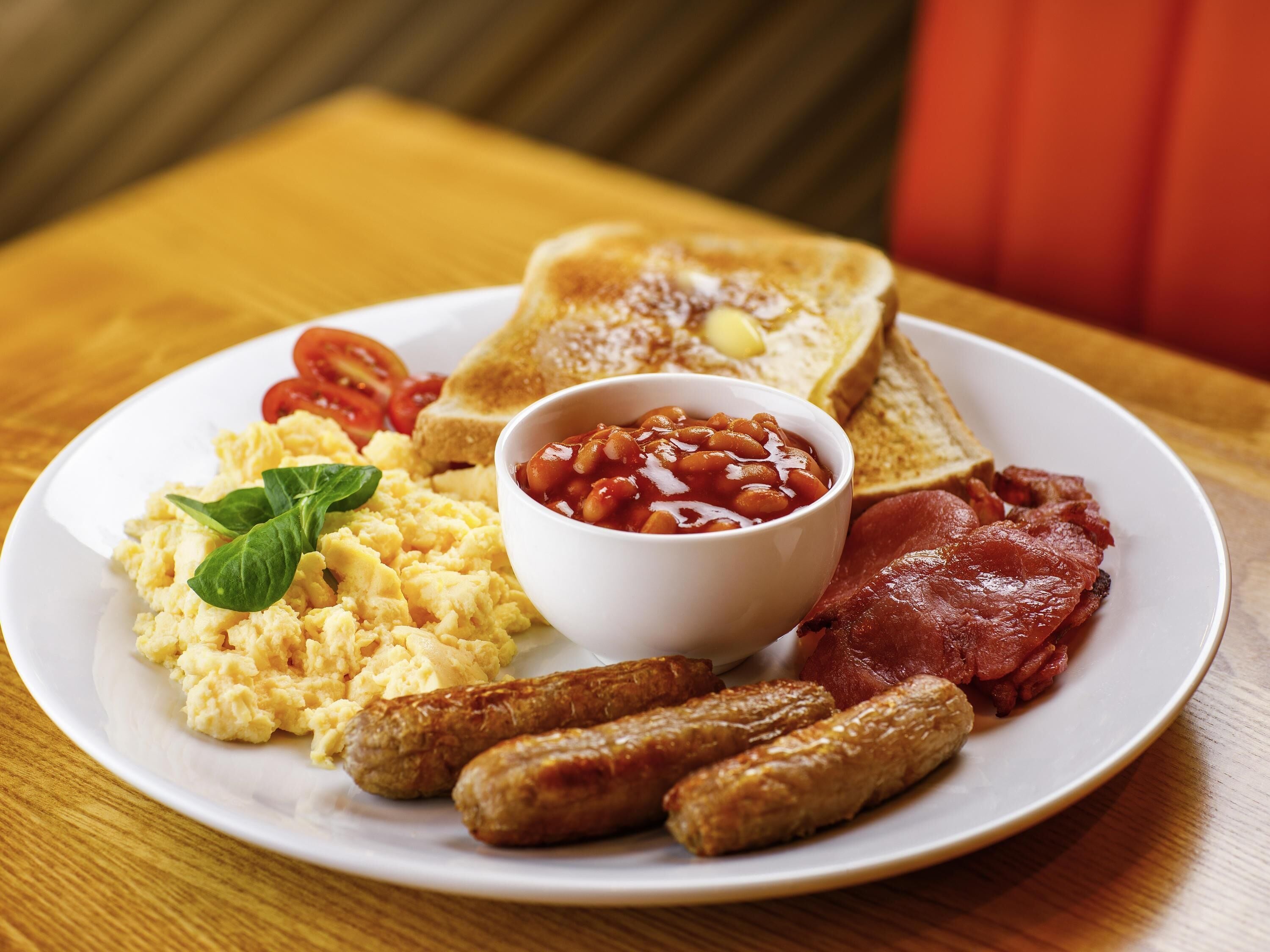 A plate of breakfast food including scrambled eggs, sausages, toast, beans, and bacon.