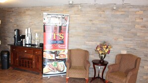 A lobby with a brick wall, a coffee station, two armchairs, and a poster advertising a classic grill. - Quality Inn & Suites Edmonton International Airport (Leduc)