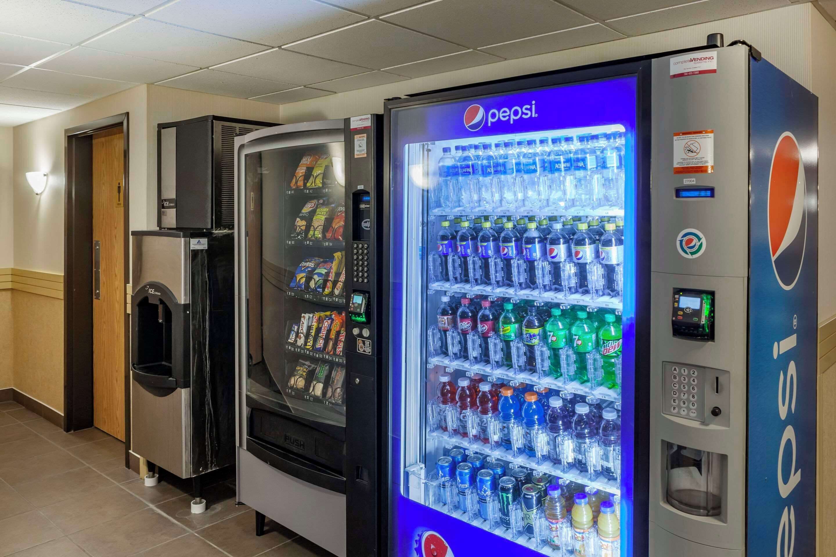 Zona de máquinas expendedoras con un refrigerador de Pepsi repleto de bebidas y aperitivos.