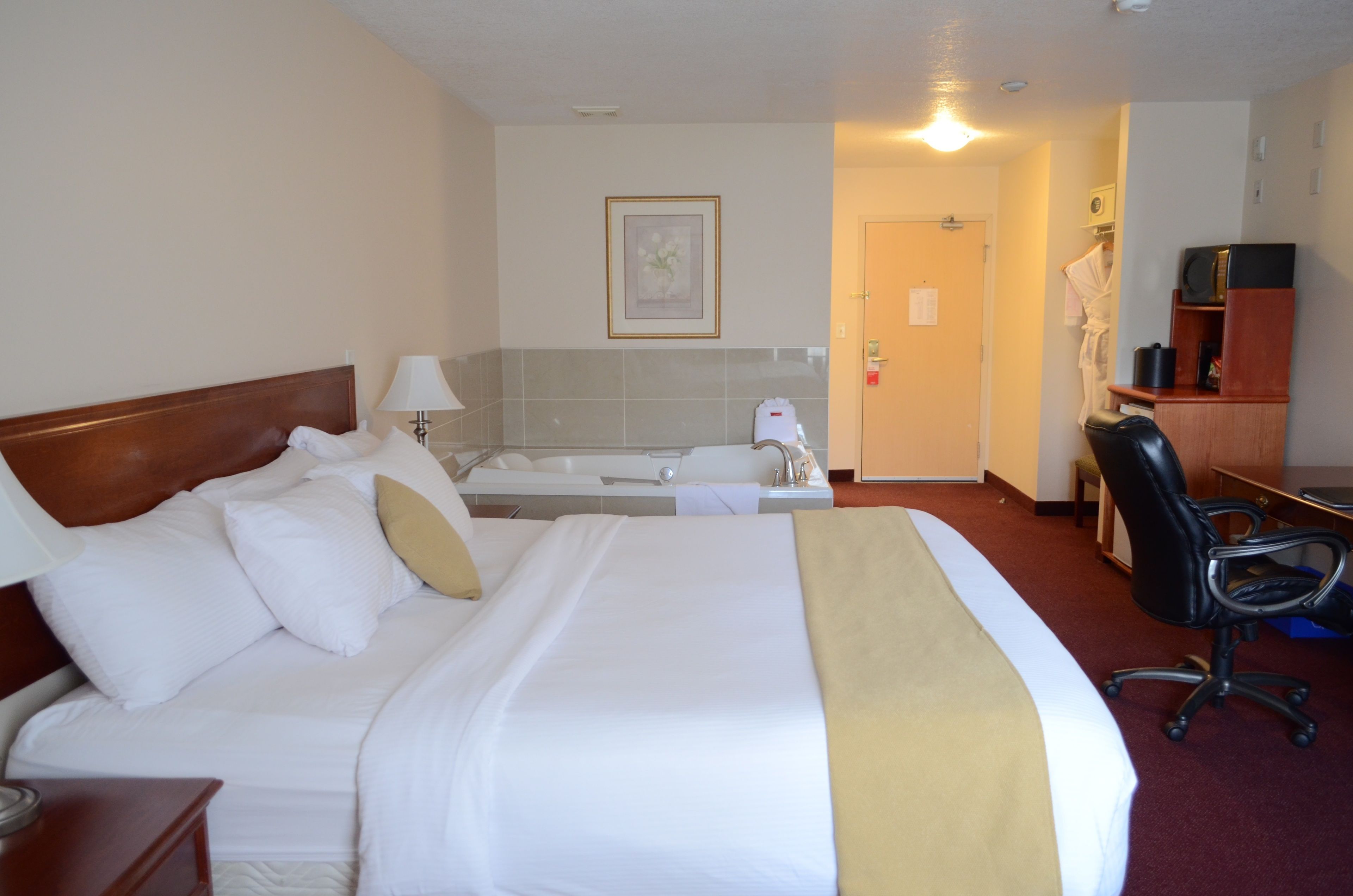 A hotel room with a large bed, a desk, a chair, a bathtub, and a small bathroom.