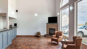 A modern living room with a fireplace, seating area, and a large window overlooking a parking area. - Quality Inn & Suites Edmonton International Airport (Leduc)