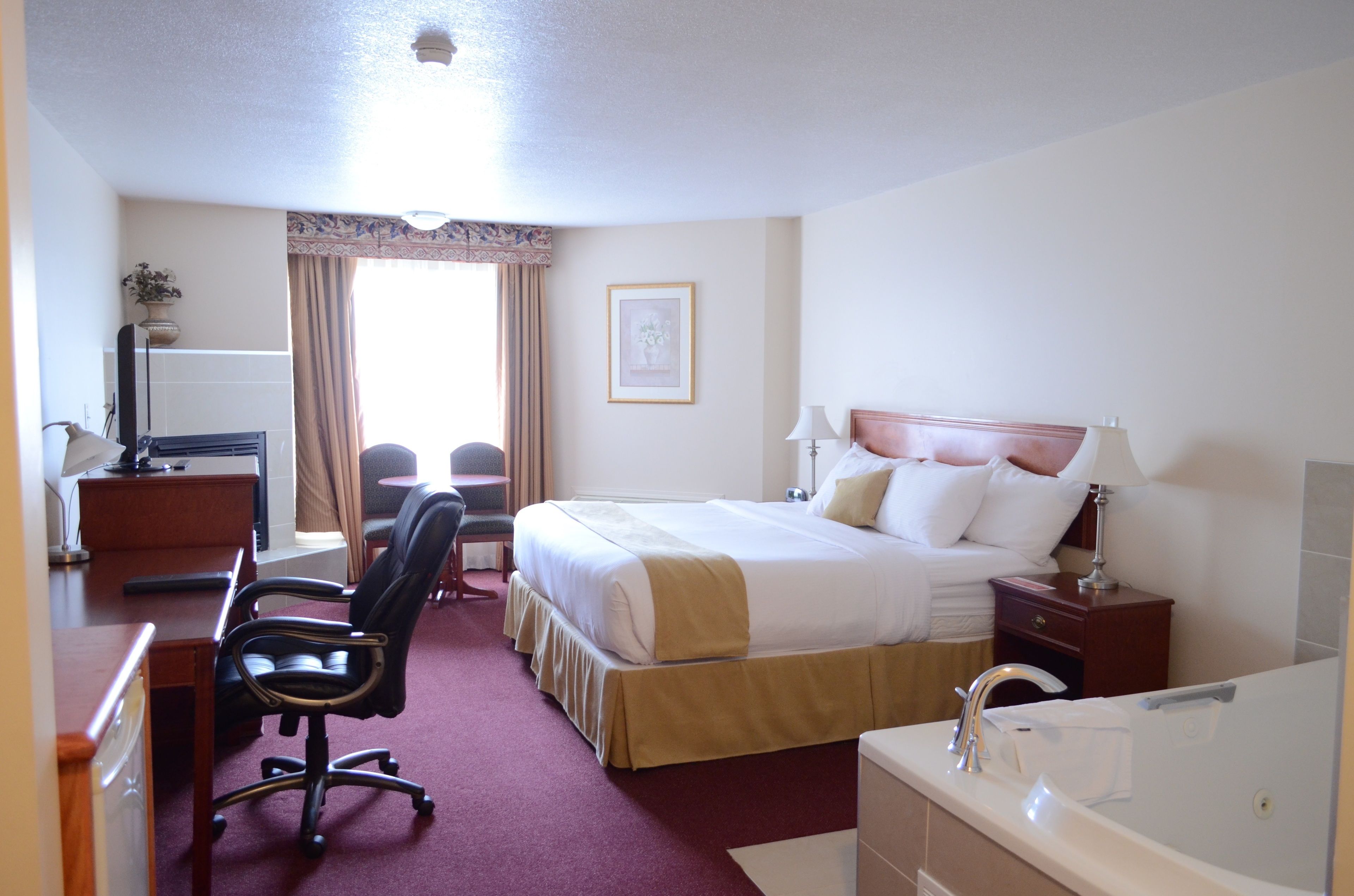 A hotel room with a bed, desk, chair, and a bathroom with a bathtub.