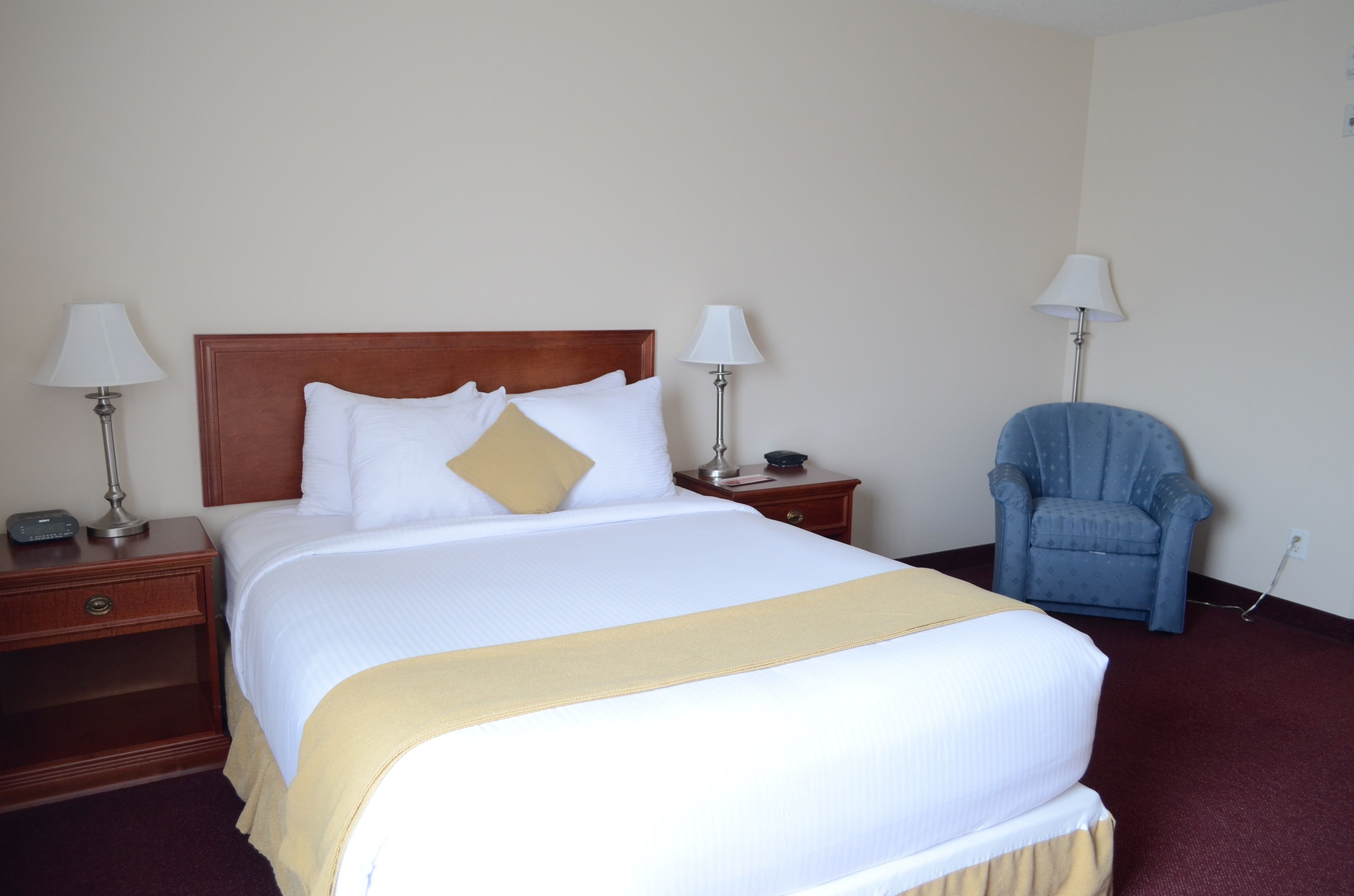 A neatly made bed with a wooden headboard, two bedside tables with lamps, and a blue armchair.