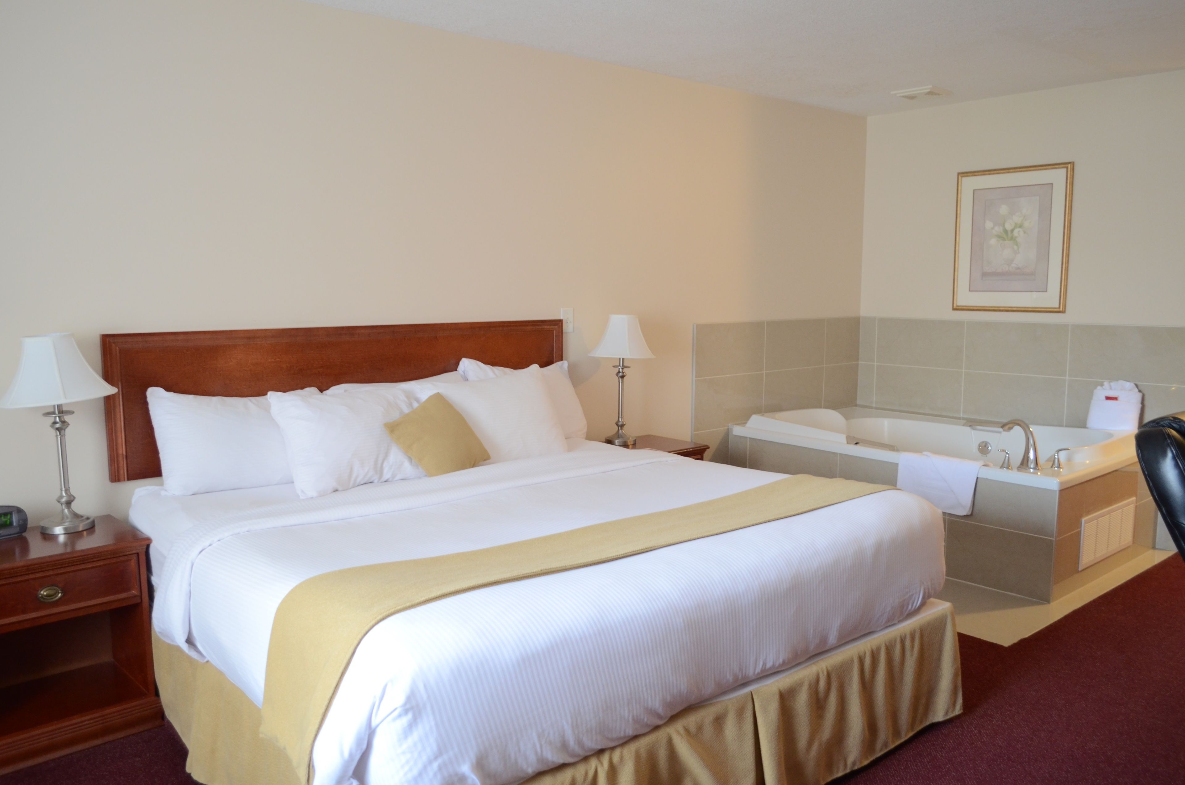 A hotel room with a large bed, a bedside table with a lamp, a bathroom with a bathtub, and a framed picture on the wall.