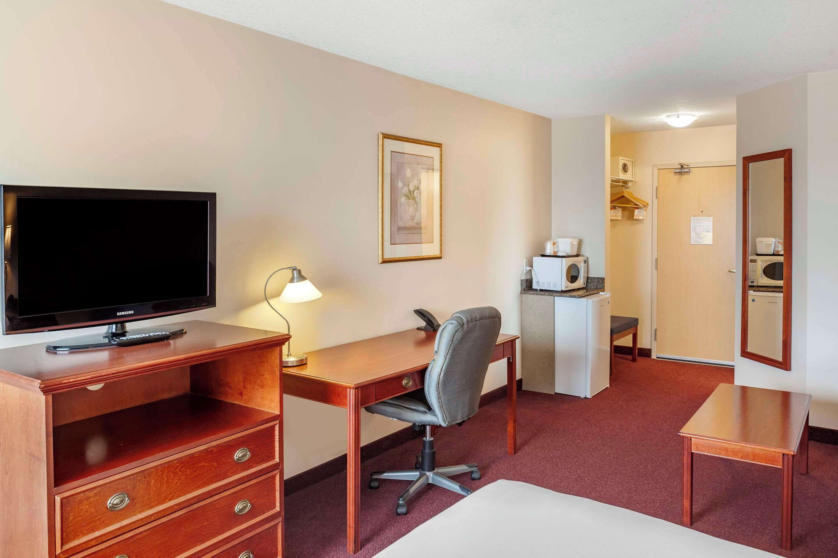 A hotel room with a TV, desk, chair, dresser, and a microwave.