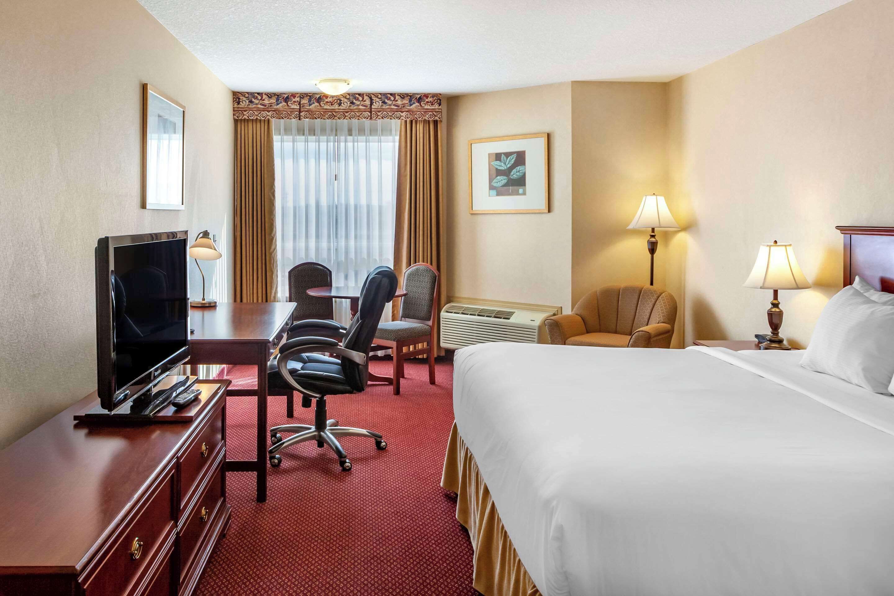 A hotel room with a bed, desk, TV, chairs, and lamps.