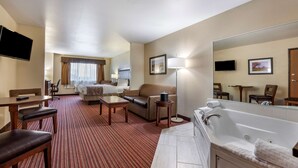 Habitación de hotel con sala de estar, sofá, mesa de centro, televisor, un espejo grande, bañera y piso alfombrado.