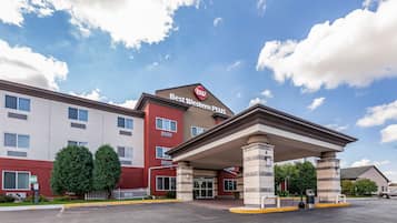 A Best Western Plus hotel with a covered entrance, a parking lot, and a clear blue sky with clouds.