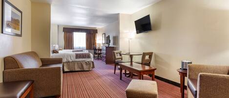 A hotel room with a bed, a sofa, a desk, a chair, and a TV mounted on the wall.