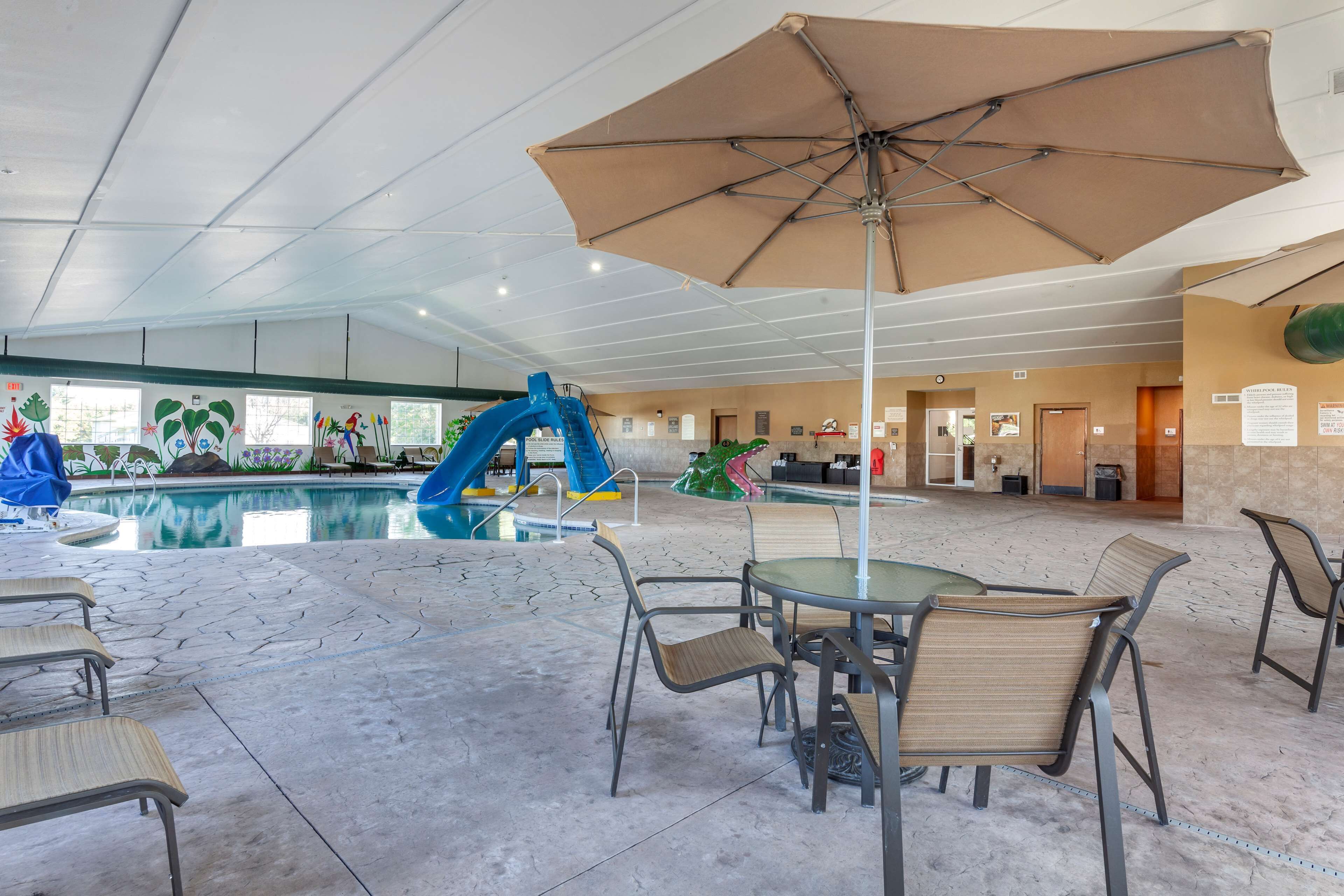 A pool area with a blue slide, outdoor seating, and a large umbrella.