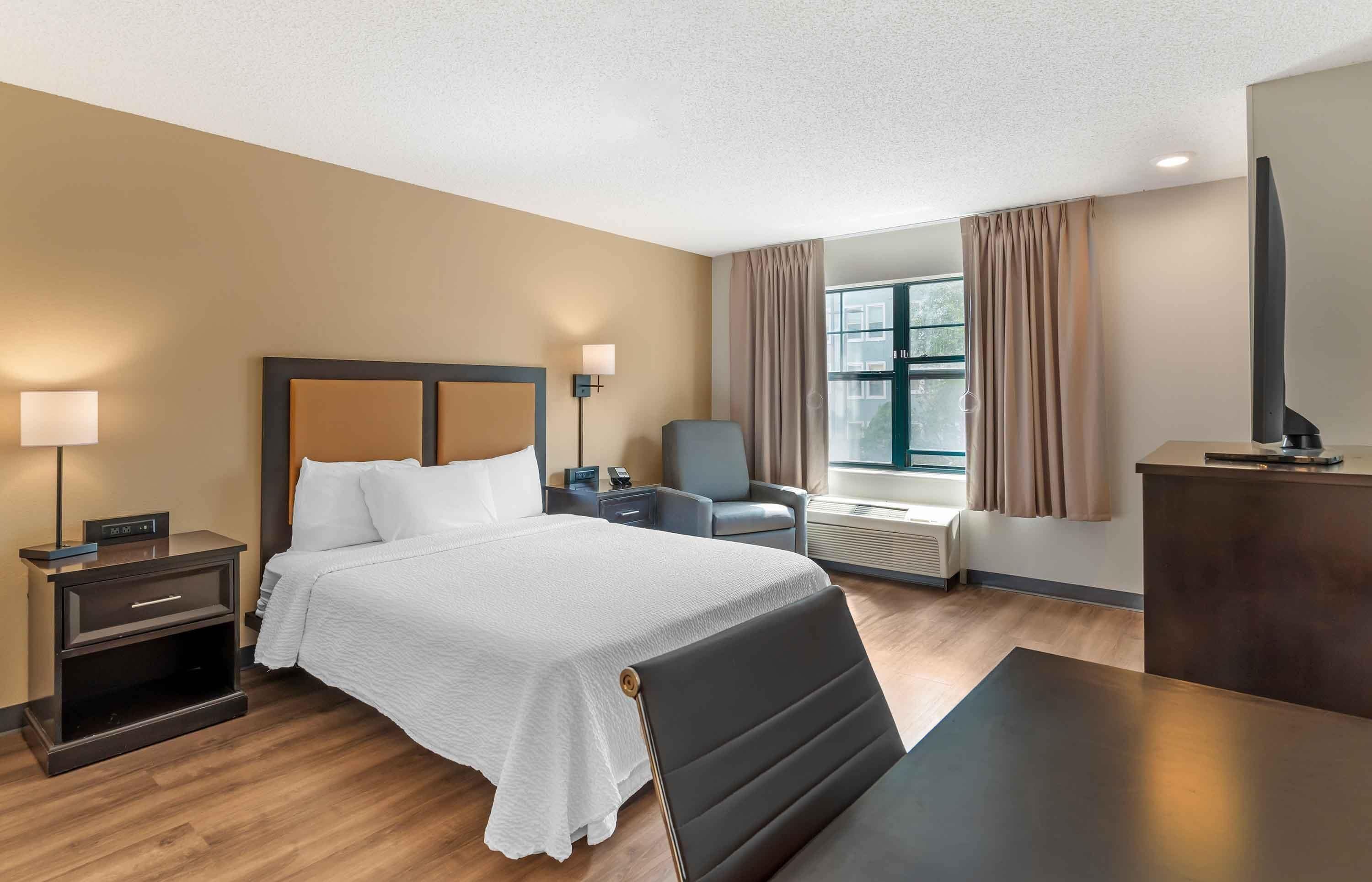 Une chambre d’hôtel comprenant un lit, des tables de chevet, un bureau, une chaise, une télévision et une fenêtre avec des rideaux.