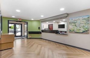 A reception area with a wooden desk, a reception counter, an exit sign, and a wall-mounted TV.