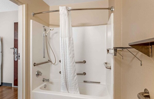 A walk-in shower with a white curtain, a handheld showerhead, and a handheld scrubber.
