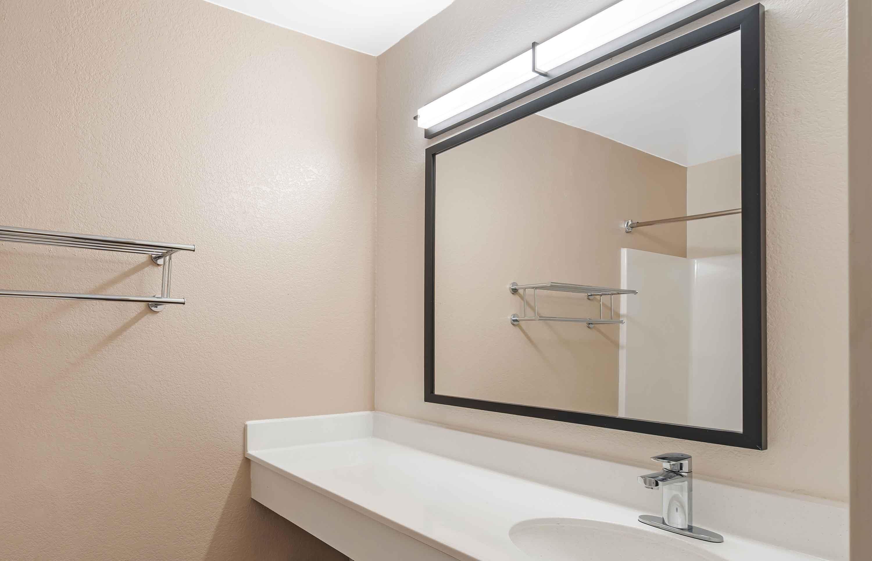 A bathroom with a white sink, a large mirror, and a towel rack.
