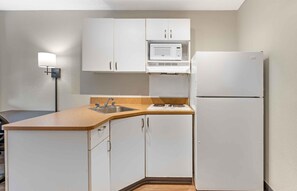 A compact kitchen with white cabinets, a microwave, a refrigerator, a sink, and a countertop.