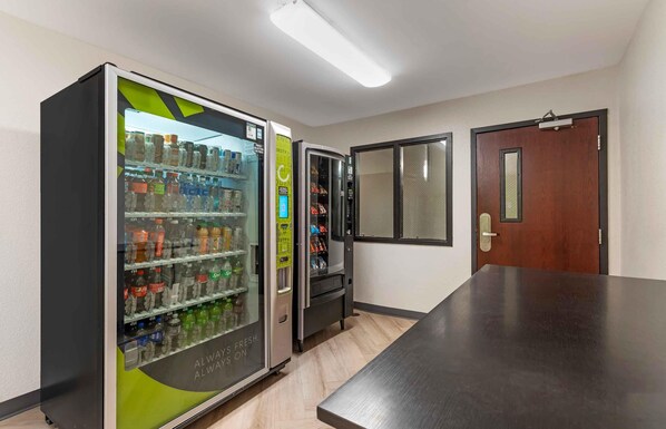 A room with a long table, two vending machines, a door, and a window.
