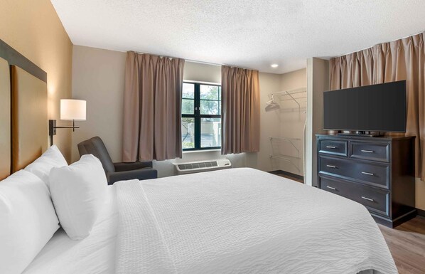 A hotel room with a large bed, a desk, a chair, a TV, and a wardrobe.