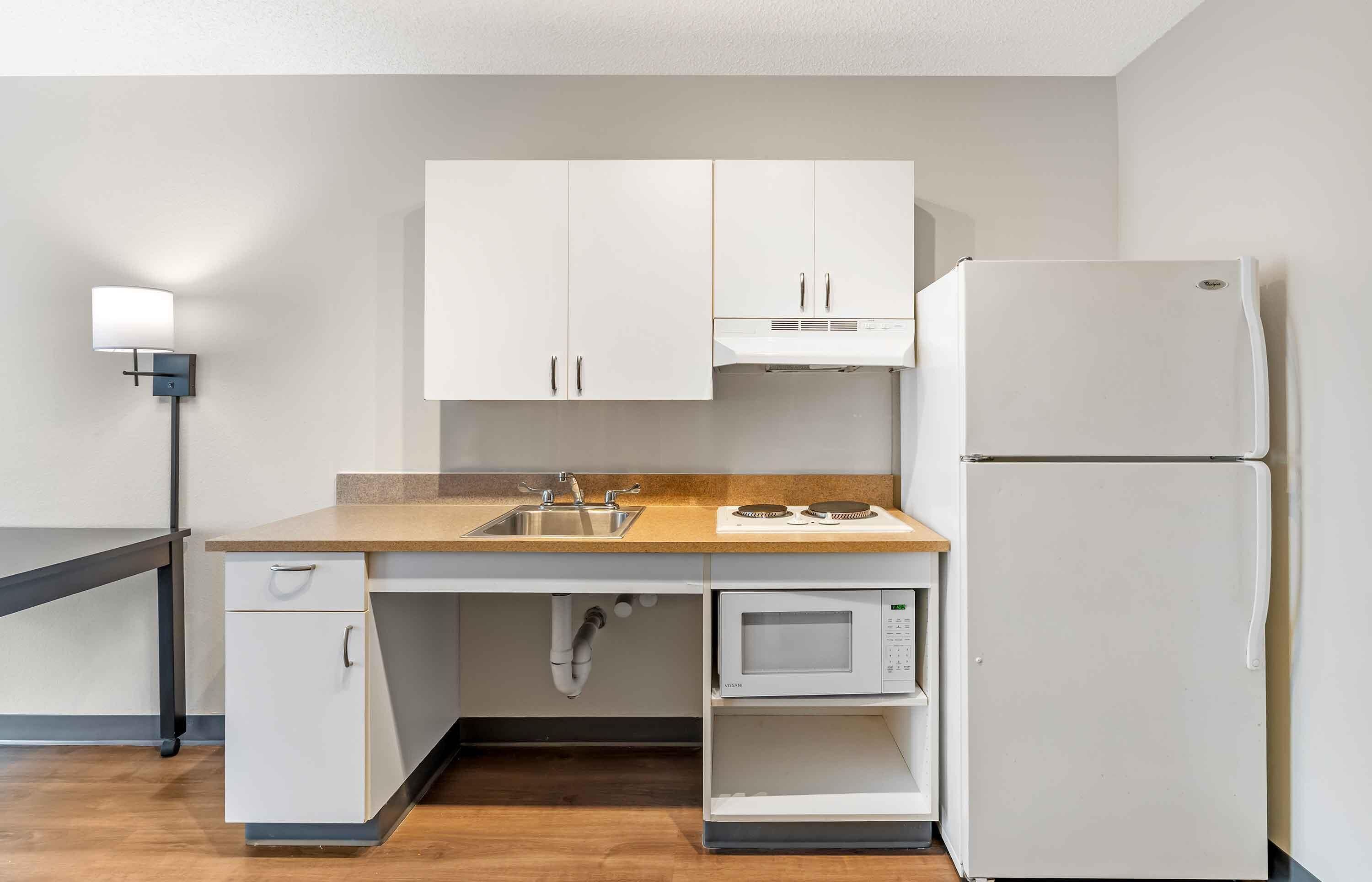 A compact kitchen with white cabinets, a microwave, a sink, and a refrigerator.