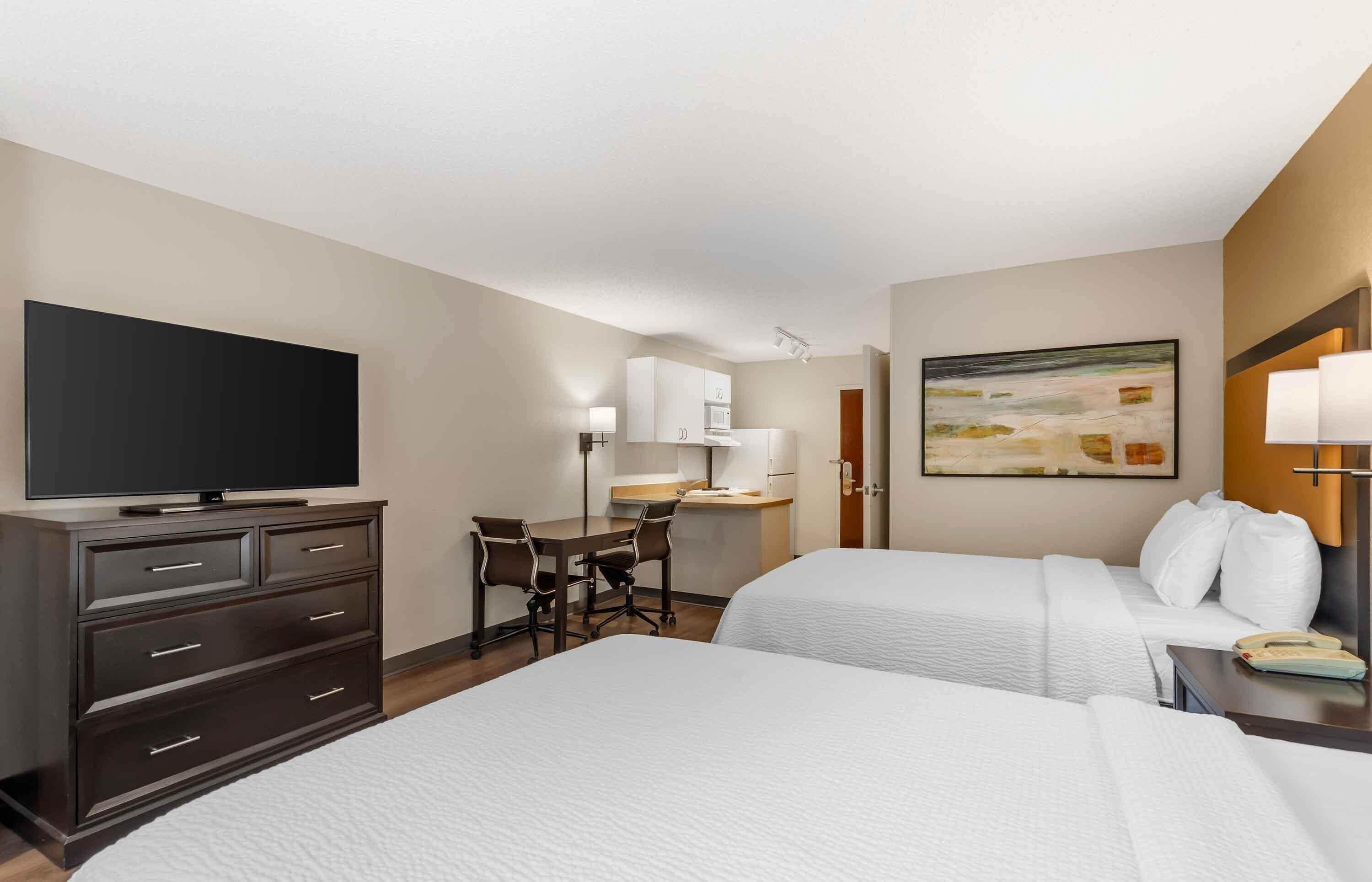A hotel room with two beds, a desk, a TV, and a painting on the wall.