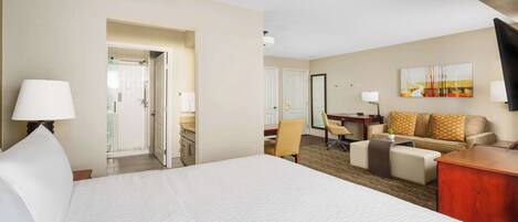 A hotel room with a large bed, a desk, a sofa, and a television.