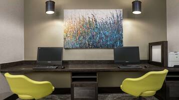 Un espacio de trabajo de hotel con dos escritorios, dos monitores y dos sillas amarillas.