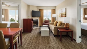 Habitación de hotel con televisor de pantalla plana, chimenea, sofá, mesa de comedor y vistas al exterior.