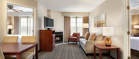 A hotel room with a dining table, a sofa, a TV, a fireplace, and a door leading to another room.