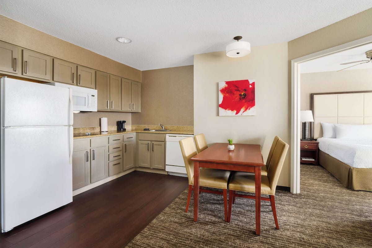 A compact hotel room with a kitchenette, a dining area, and a bed.