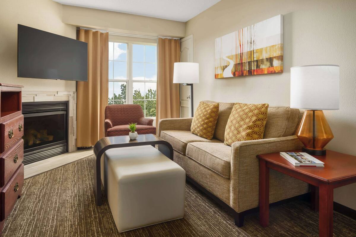 A hotel room with a fireplace, a sofa, a coffee table, a TV, and a painting on the wall.