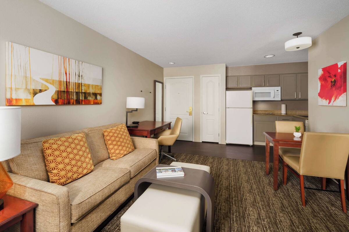 A modern hotel room with a living area, kitchenette, and a dining area.