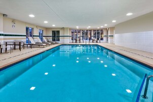 Una piscina interna con sedie a sdraio e tavoli, circondata da pareti piastrellate e ampie finestre.
