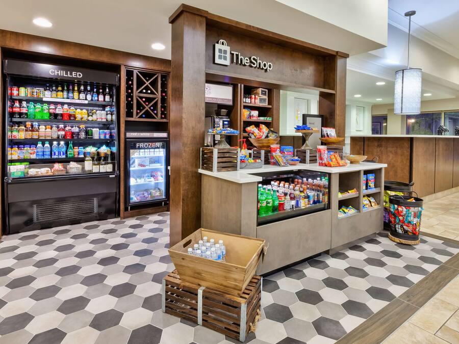 Un hall d’hôtel comprenant un kiosque intitulé « La Boutique », des distributeurs de boissons fraîches et un présentoir de collations.