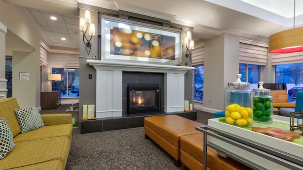A modern living room with a fireplace, a sofa, a coffee table, and a TV mounted above the fireplace. - Hilton Garden Inn Minneapolis - Maple Grove (Maple Grove)