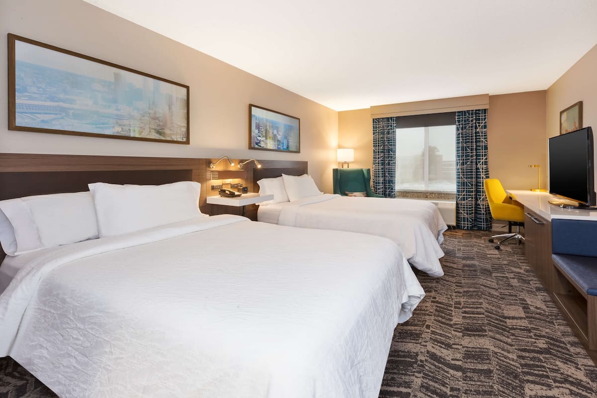 A hotel room with two beds, a desk, a television, and a cityscape view.