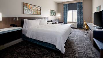 A hotel room with a large bed, a desk, a television, and artwork on the walls.