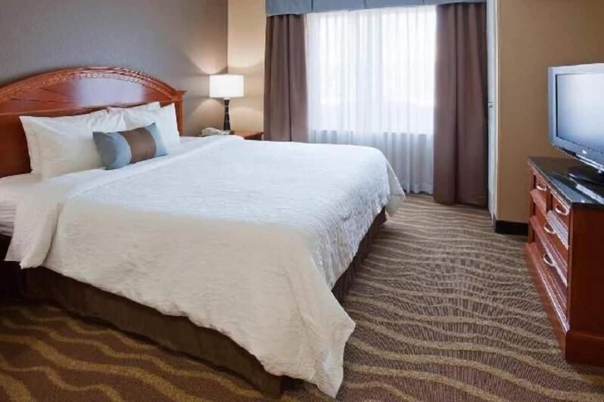 A hotel room with a large bed, a television, a nightstand, and a window with curtains.