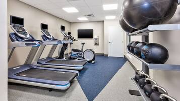 Une salle de sport équipée de tapis de course, d’un vélo d’appartement et de matériel de musculation.